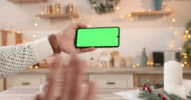 Крупный план белого мужчины рука держит черный смартфон с зеленым экраном, стоя в украшенном доме в канун Рождества сотовый телефон с хрома ключ в руках человека на праздники Технология концепция — стоковое видео