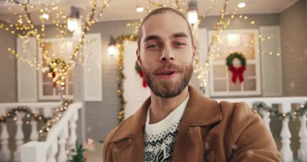 POV of happy handsome Caucasian young man standing on decorated christmas street in city and video chatting in festive mood sending best wishes on New Year. Christmas greetings Close up portrait — Stock Video