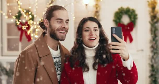 Close-up portret van gelukkige blanke jonge glimlachende getrouwde familie koppel spreken op video oproep in feestelijke stemming op de smartphone op de versierde straat in de stad. Kerstgroeten concept, Nieuwjaar — Stockvideo