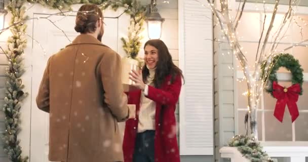 Happy Caucasian young wife and husband exchanging christmas gifts while standing outdoors on decorated street in festive mood. Woman receive present from beloved man on New Year Eve — Stock Video