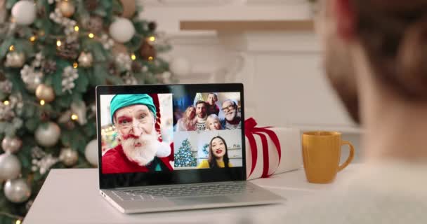 Sopra vista spalla di uomo che parla in videoconferenza sul computer portatile con coppia caucasica, asiatico femmina e vecchio Babbo Natale uomo. Amici e parenti di razze miste che parlano in vacanza su più video — Video Stock