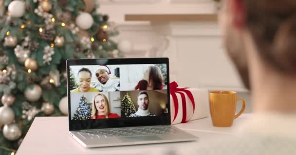 Przez ramię widok młodego faceta w urządzonym pokoju rozmowy wideo na laptopie z wielu etnicznych przyjaciół Boże Narodzenie. Młodzi ludzie rozmawiający w Wigilię na wielu czatach wideo. Zamknij się. — Wideo stockowe