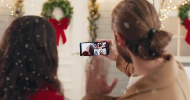 Κοντινό πλάνο της οθόνης smartphone με online τηλεδιάσκεψη βιντεοκλήση με διαφορετικούς ανθρώπους. Πίσω μέρος της μαγνητοσκόπησης ζευγάρι στο κινητό με τους φίλους και τους συγγενείς την παραμονή των Χριστουγέννων στέκεται στο δρόμο — Αρχείο Βίντεο