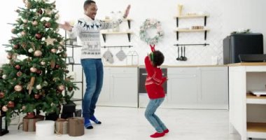 Afrikalı Amerikalı baba ve küçük çocuk Noel arifesinde yeni yıl ağacıyla süslenmiş modern ev mutfağında Xmas müziği ve dans dinlerler. Mutlu aile boş zamanlarının ve eğlenceli tatil konseptinin tadını çıkarırlar.
