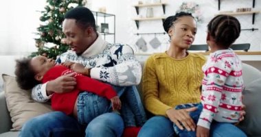 Mutlu ailelerin Noel 'de dekore edilmiş modern evlerde oturması. Anne başka bir çocukla konuşurken mutlu baba çocukla oynuyor. Aile tatili konsepti. Yeni yıl havası