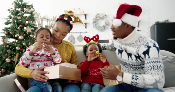 Ritratto di curiosi bambini afroamericani aprire scatole regalo mentre seduti con i genitori felici insieme a casa decorata vicino a grazioso albero di Natale Capodanno. Feste celebrazione Natale concetto presente — Video Stock