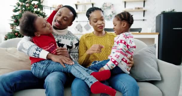 Blisko szczęśliwej afroamerykańskiej rodziny w dobrym nastroju siedzi w urządzonym pokoju w Wigilię. Rodzice z dziećmi rozmawiają i bawią się razem w wakacje. Koncepcja świąt. Nastrój noworoczny — Wideo stockowe