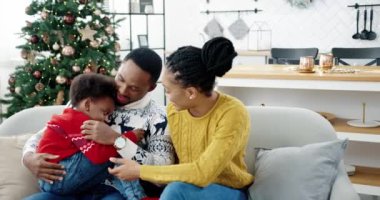 Mutlu Afro-Amerikan aile portresi Noel arifesini evde, Noel süslemeli odada, anne ve babayı severek ve yeni yıl ağacının yanındaki kanepede çocuk oyunu oynayarak geçiriyoruz. Tatil kavramı
