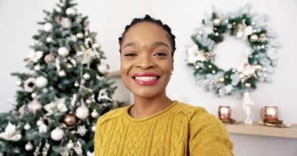 Pov von glücklichen afroamerikanischen Frau zu Hause mit geschmücktem Weihnachtsbaum mit Lichtern Video-Chat im Internet und Urlaubsgrüße an Freunde und Verwandte. Heiligabend. Feiertagsstimmung — Stockvideo