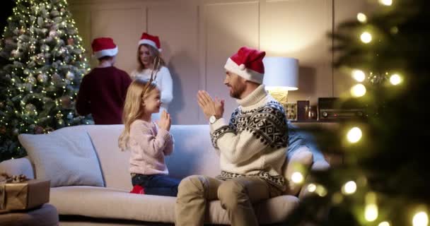 Cheerful Caucasian little girl playing with caring loving dad at home on christmas eve. Mom and son decorating xmas tree on background. Christmas preparation. Happy holiday concept — Stock Video