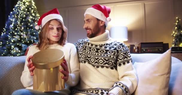 Κοντινό πορτρέτο της καυκάσιας χαρούμενης συζύγου που λαμβάνει και ανοίγει χριστουγεννιάτικο κουτί δώρου από τον σύζυγο στο σπίτι. Νοιάζεσαι για τον ευτυχισμένο άντρα που δίνει δώρο στη γυναίκα και αγκαλιάζει την που δείχνει αγάπη. Xmas παρουσιάζει — Αρχείο Βίντεο
