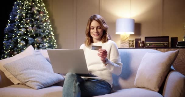 Wesoły uśmiech biała piękna kobieta kupuje w Internecie xmas prezenty płacąc kartą kredytową za pomocą laptopa w przytulnym urządzone domu. Sprzedaż świąteczna i rabaty. Wakacyjne zakupy — Wideo stockowe