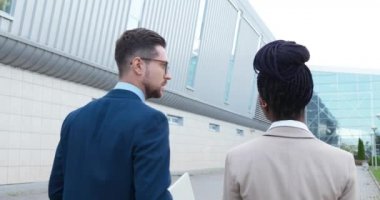 Açık havada yürüyen ve iş hakkında konuşan melez iş adamları ve iş kadınları. Çok ırklı iş adamı ve iş kadınının arka planda gezip iş görüşmesi.