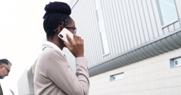 Zadní na Afroameričanka mladá obchodnice v brýlích procházející se po ulici pracovat v obchodním centru, mluvit na mobilním telefonu. Stylová žena, která se ráno prochází a mluví na mobilu. Zadní pohled — Stock video