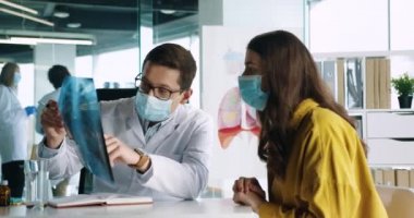 Tıbbi maske takmış, beyaz kadın hastayla konuşan, röntgen taramasını açıklayan ve tartışan yakışıklı bir erkek doktor. Sağlık sigortası konsepti. Coronavirus covid-19
