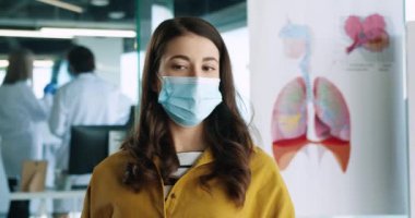 Tıbbi maskeli güzel beyaz kadın portresi. Doktor randevusunda hastane dolabında oturmuş doktorla sağlık sorunlarını konuşuyor. Coronavirus konsepti
