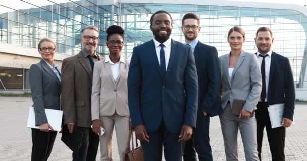 男性と女性の会社の労働者の彼のチームとアフリカ系アメリカ人の若いボスの成功の肖像画。ビジネスセンターで屋外カメラに笑顔の混合レースビジネスマンやビジネス女性. — ストック動画