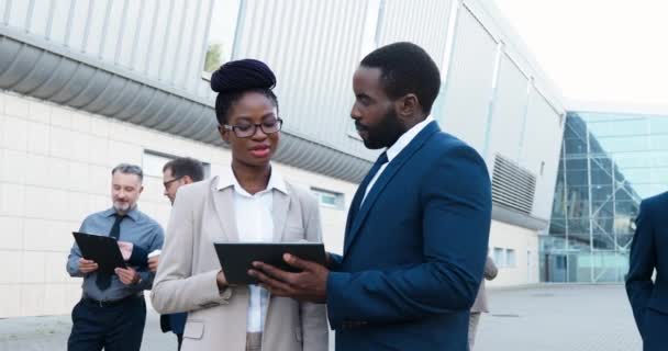 Afro-Amerikalı genç iş kadını ve işadamı sokakta duruyor ve ellerinde tablet cihazla çalışmaları tartışıyorlar. Karışık ırktan kadın ve erkek çalışma projeleri hakkında konuşuyor. Tavsiye vermek. — Stok video