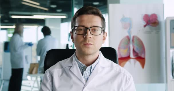 Close up portrait of handsome Caucasian male physician in glasses sitting in hospital office at workplace looking at camera and speaking on medical consultation. Healthcare concept. Doctor appointment — Stock Video
