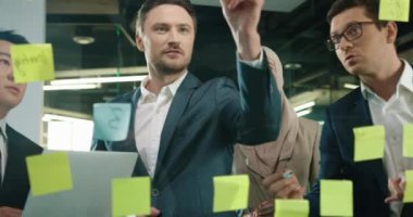 Modern ofiste çalışan çok ırklı profesyonel yöneticilere yakın çekim. Asyalı bir adam dizüstü bilgisayarda yazarken beyaz bir erkek ahır cam tahtaya yazı yazıyor ve konuşuyor. Girişim konsepti