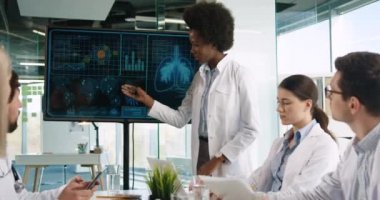 Karışık ırk erkek ve kadın doktorlar hastane ofisinde oturup dijital ekrana bakıyorlar. Afro-Amerikan tıp çalışanı pulmon hastalığı hakkında konuşuyor covid-19 koronavirüs salgını