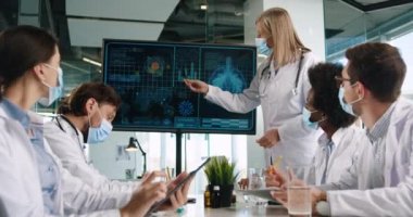 Maskeli melez ırklar hastanede toplanıp dijital ekrana bakıyorlar ve tıkaç enfeksiyonunu tartışıyorlar. Tablet yazıp Coronavirus hakkında bilgi yazıyorlar.