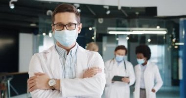 Kafkas doktor portresi, tıbbi maske takmış hastanede kameraya bakıyor. Sağlık uzmanı arka planda tablet kullanıyor. Coronavirus enfeksiyonu konsepti