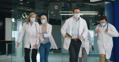 Acil bir durumda hastanede koşan, tıbbi maskeler takan melez erkek ve kadın doktorlar. Klinikte acil Coronavirus vakası. İş yerinde panik. Covid-19 salgın konsepti
