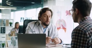 Steteskopu olan yakışıklı yetişkin erkek doktorun, iş yerindeki hastanede hasta adamla görüşürken çekilmiş portresi. Sağlık sigortası konsepti. Tıbbi tavsiye. Tıp Merkezi