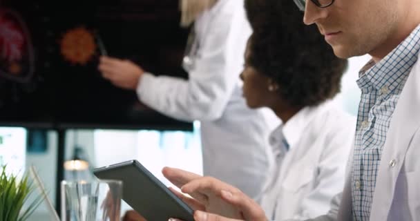 Primer plano de diversos médicos de razas mixtas mirando la presentación de la pantalla digital sentado en la reunión y discutiendo las estadísticas de covid-19 en el hospital y escribiendo en la tableta. Coronavirus Concepto de salud — Vídeo de stock