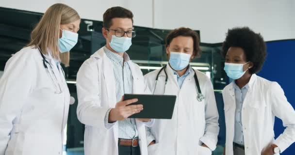 의료용 마스크를 쓴 남녀 혼혈 의사들은 병원에 서 있는 동안 코로나 바이러스 감염에 대해 논의하고 있다. 의료 전문가들이 일하는 모습. 격렬 한 세계적 유행병 19 — 비디오