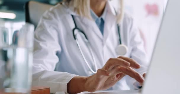 Zbliżenie na piękną starszą, zajętą białą lekarkę siedzącą w biurze szpitalnym, pracującą, podsłuchującą i piszącą na laptopie w miejscu pracy. Pracownik służby zdrowia pisze SMS-y na komputerze. Koncepcja pracy — Wideo stockowe