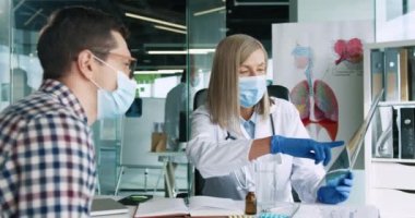 Klinikte kıdemli kadın doktorla muayenede olan genç bir erkek hastanın portresi. Tıbbi maskeli bir sağlık görevlisi hastayla röntgen taramasını tartışıyor.