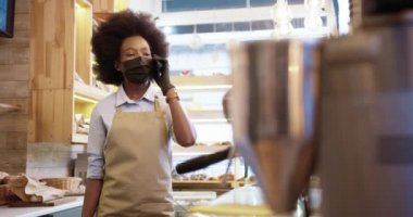 Güzel Afrikalı Amerikalı genç kadın satıcı pastanede duruyor ve cep telefonuyla konuşuyor. Küçük bir kafede akıllı telefondan konuşan kadın fırın işçisi. Görev konsepti
