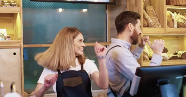 Primer plano de alegres jóvenes trabajadores y trabajadoras en delantales en el trabajo de buen humor divirtiéndose y bailando en la cafetería. Felices propietarios de panaderías celebrando la reapertura interior. Concepto empresarial — Vídeo de stock