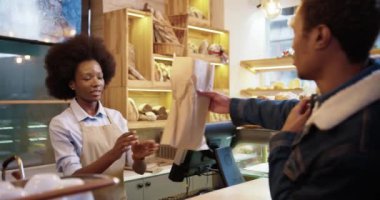 Afro-Amerikalı güzel mutlu kadın satıcının kapanışı fırında taze ekmek veriyor. Erkek müşteriler fırından aldıklarında kredi kartıyla ödeme yapıyorlar. Yiyecek konsepti