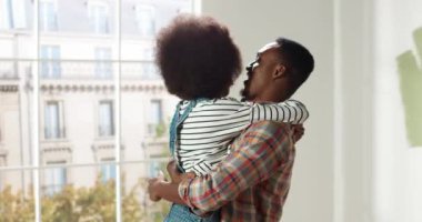 Afro-Amerikan genç kadın ve kocanın ev onarımı sırasında odada durarak kucaklaşmalarının portresi. Daire tadilatı ve iyileştirme. Yeni evi dekore ediyorum. Mutlu aile kavramı