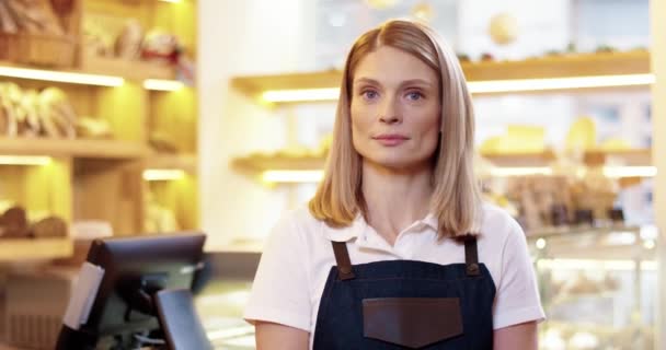 Close up of joyful Caucasian beautiful young female seller standing in own bakery, looking at camera and smiling in good mood. Bakehouse woman owner at work. Businesswoman concept — Stock Video