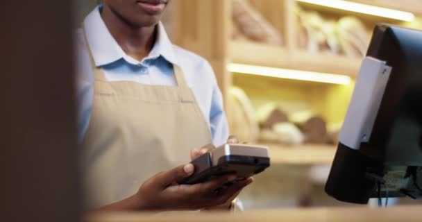 Közelkép afro-amerikai női eladó eladási pékség bolt segítségével eszköz, hogy a fizetés. Kaukázusi ügyfél kézzel fizet hitelkártyával, miközben vásárol a bakehouse-ban. Üzleti koncepció — Stock videók