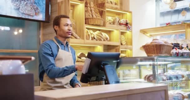 アフリカ系アメリカ人の男性の売り手の肖像は、顧客と話を自分のパン屋でベーキングを販売している。パン屋での女性客のリア。小規模事業。食品業界のコンセプト — ストック動画