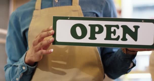 Nahaufnahme von afroamerikanischen männlichen Händen, die im Backshop ein Schild mit der Aufschrift "Open" in der Hand halten. Wiedereröffnung des Geschäfts. Kleinunternehmen. Mann Arbeiter Unternehmer hält Open Card drinnen. — Stockvideo