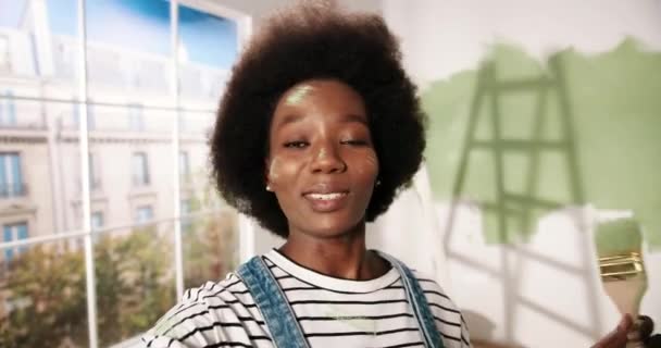 POV of cheerful African American pretty young female with painted face standing in room renovating home and talking on video call in good mood. Renovating and redesigning house Repair concept Close up — Stock Video