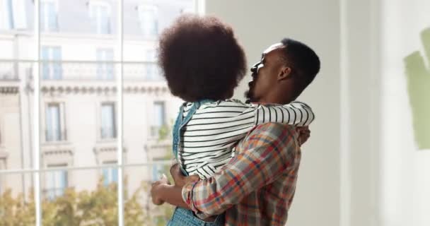 Retrato de alegre afro-americano jovem esposa e marido abraçando de pé no quarto durante o reparo em casa. Renovação e melhoria de apartamentos. A decorar uma casa nova. Conceito de casal feliz família — Vídeo de Stock