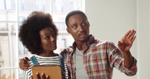 Primer plano retrato de linda esposa afroamericana feliz y marido tocando en el dispositivo de la tableta en busca de decoración para el nuevo apartamento discutiendo el rediseño de la casa. Reparación y mejoras en el hogar — Vídeos de Stock