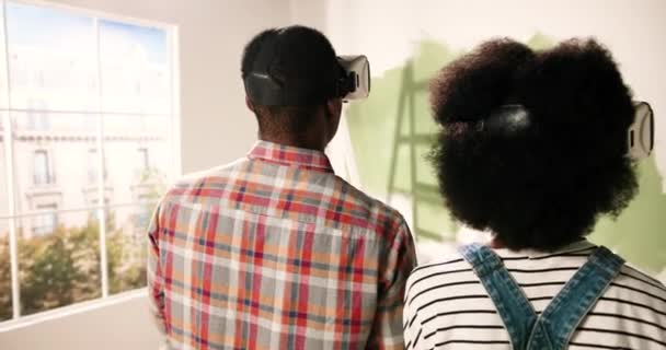 Chiudete. Posteriore della coppia di sposi afroamericani in piedi in camera durante la ristrutturazione della casa indossando occhiali VR e guardando il nuovo design rinnovato appartamento utilizzando la tecnologia futuristica realtà virtuale — Video Stock