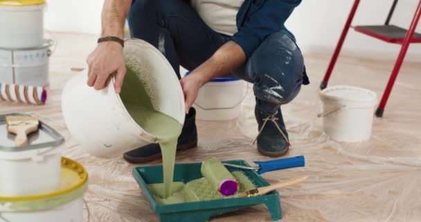 Primer plano del joven guapo caucásico vertiendo pintura verde oliva preparando para pintar paredes en la casa renovando y rediseñando la habitación. Handyman trabajando en la reparación de la redecoración del apartamento y cambio de imagen — Vídeo de stock