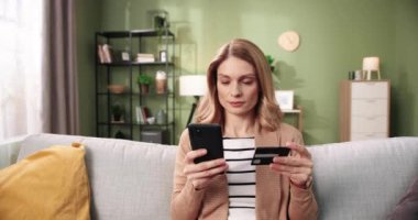 Kafkasyalı genç, güzel, mutlu yüzlü, cep telefonuyla yazı yazan, akıllı telefondan alışveriş yapan, kredi kartıyla ödeme yapan, rahat odasında oturan bir kadın. E-ticaret, online alışveriş konsepti