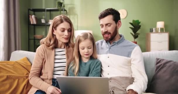 白种人快乐的年轻夫妇带着可爱的小女儿坐在家里的房间里，一边说着话，一边用笔记本电脑在网上的视频通话。家庭团聚时间 — 图库视频影像