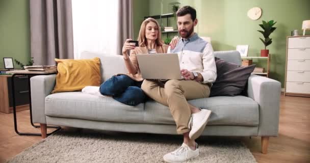 Kaukasische glückliche junge Ehepaar Frau und Mann mit Laptop eingeben, online einkaufen und im Internet kaufen, bezahlen mit Kreditkarte ruht auf dem Sofa zu Hause. E-Commerce-Konzept — Stockvideo