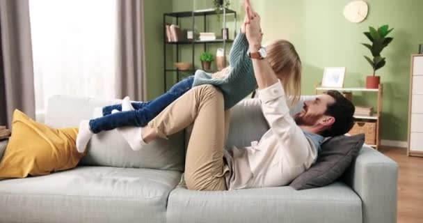 Vista lateral de alegre joven caucásico guapo padre cariñoso jugando con lindo niño hija divirtiéndose juntos haciendo llanura en el aire y riendo. Tiempo de familia en casa. Concepto de paternidad — Vídeo de stock